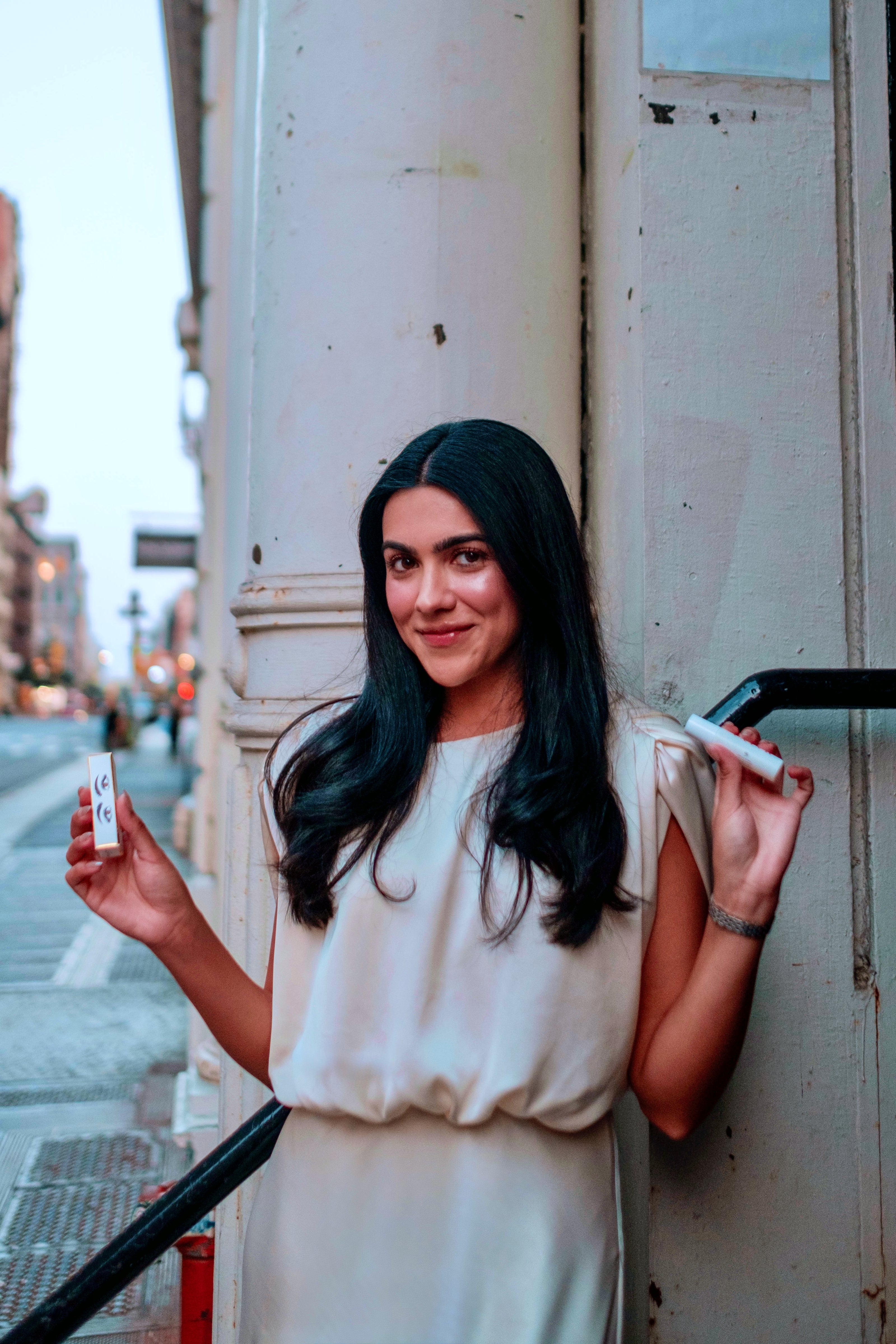 kiren ajrawat founder of halva beauty standing in soho new york city holding nourishing brow oil and packaging while smiling at the camera