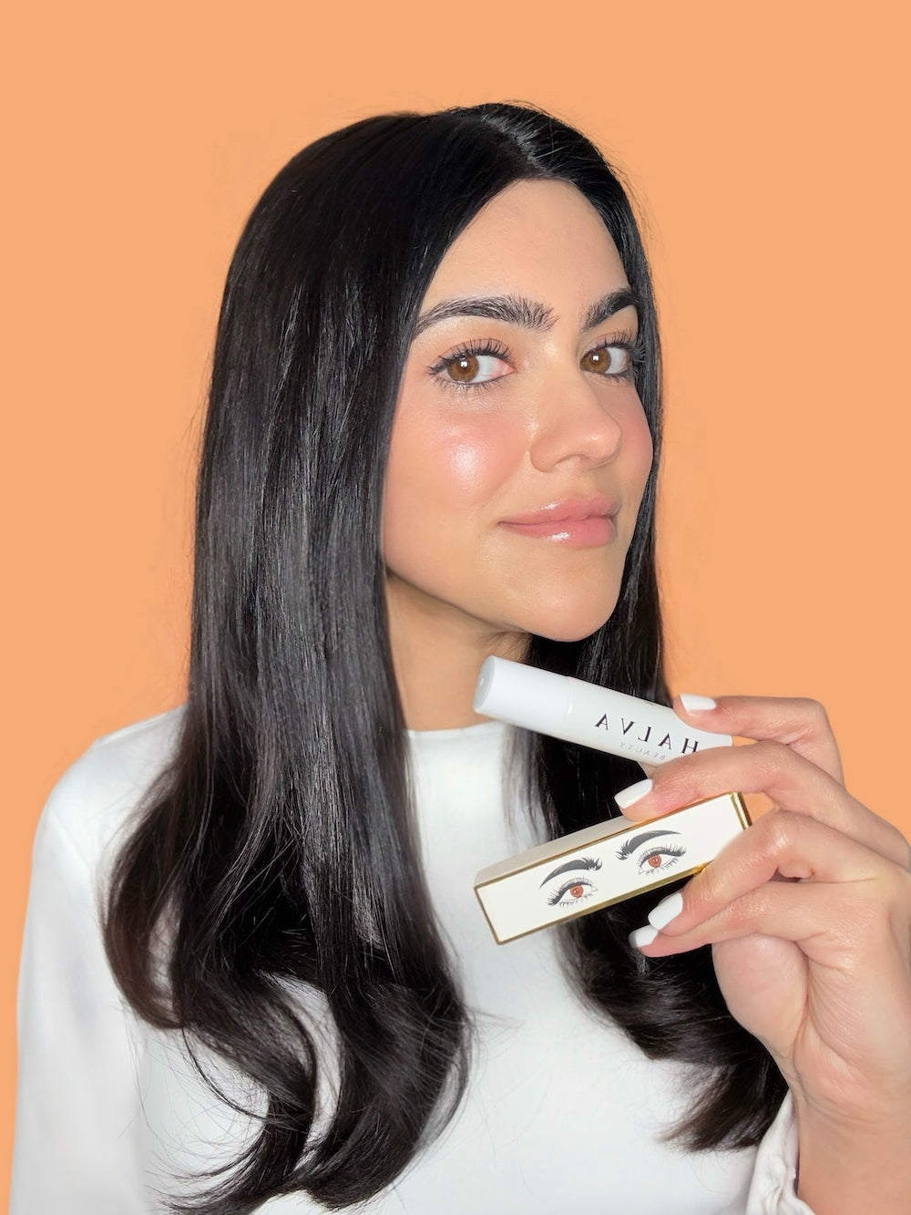 halva beauty founder kiren ajrawat holding the nourishing brow oil and its outer packaging against a warm neutral backdrop