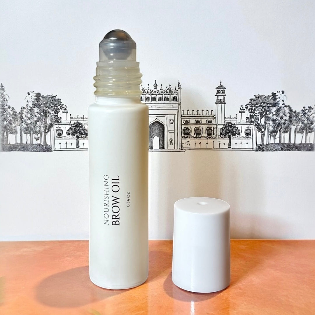 halva beauty nourishing brow oil bottle with rollerball applicator and white cap, displayed against illustrated indian architecture background on peach surface.