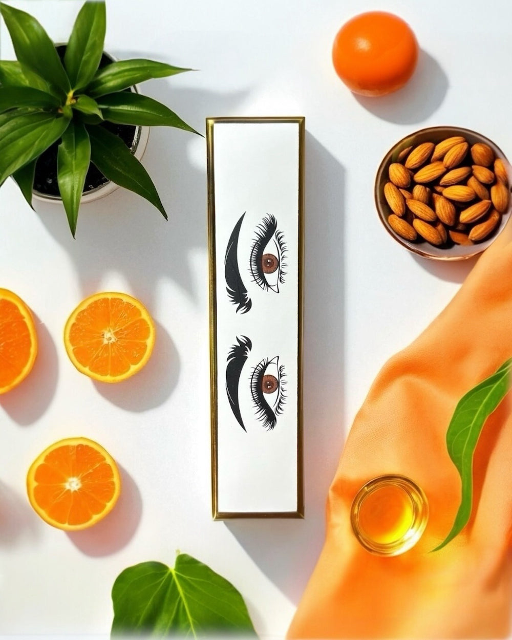 halva beauty nourishing brow oil outer packaging shown in a flat lay with illustrated eyes, almonds, oranges, moringa, babassu leaves, and oil representing natural ingredients