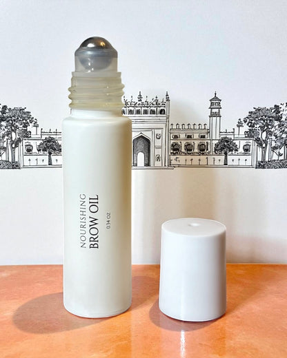 halva beauty nourishing brow oil bottle with rollerball applicator shown open beside the white cap against an illustrated indian architectural backdrop