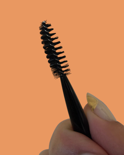 close up of halva beauty spoolie nylon bristles held by a hand against an orange background